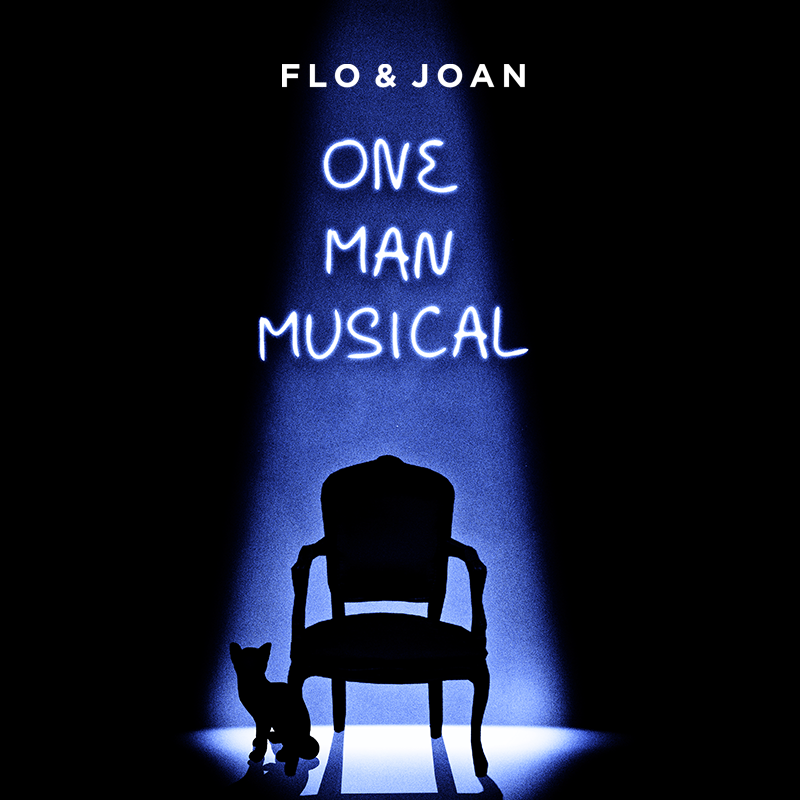 An empty chair is lit by a single spotlight. The outline of a cat can be seen at the spotlight's edge. Above the chair the show's title, One Man Musical, is written.
