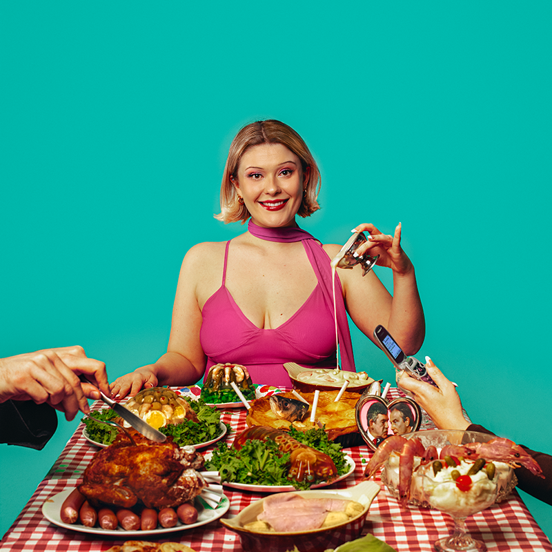 A woman dressed in pink sits at the head of a table filled with large portions of food.
