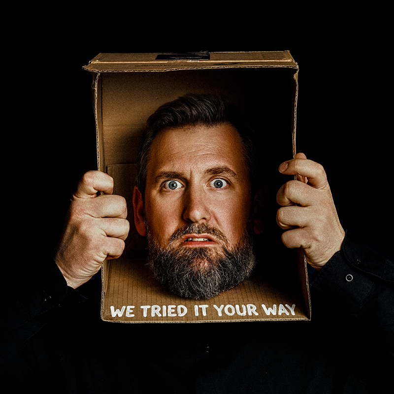 Garrett Millerick's head is stuck in a cardboard box. The words 'we tried it your way' are written across the box in white paint.