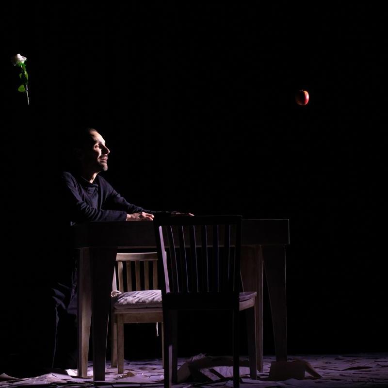 Photo showing man kneeling at a table with a rose and apple floating above