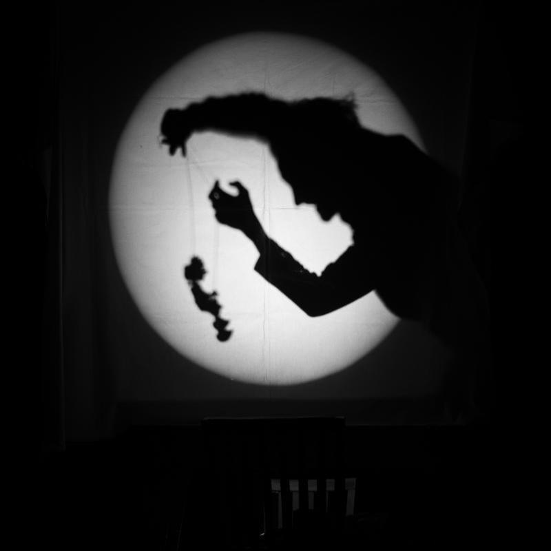 Black and white photo of a dark shadow puppeteer in a spotlight