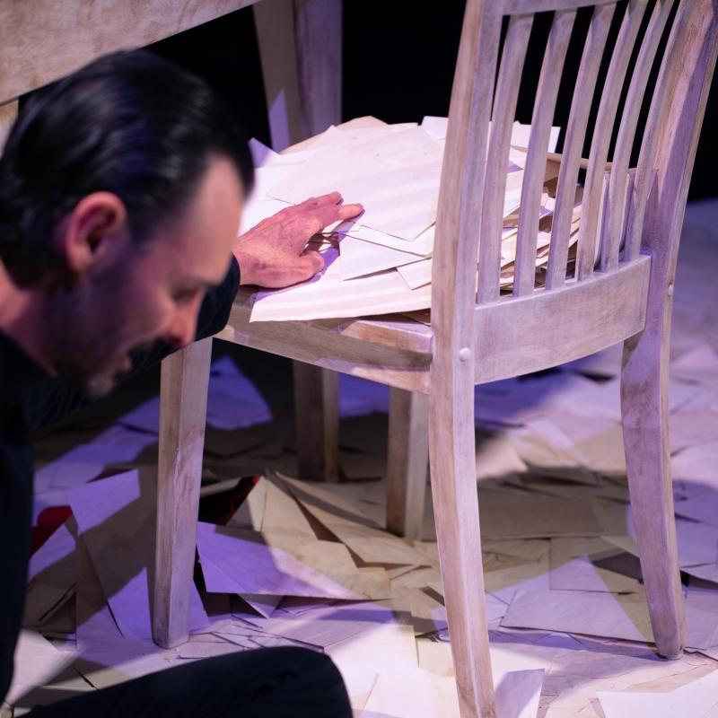 Image showing a man surrounded by pieces of paper with writing, next to a table and chair