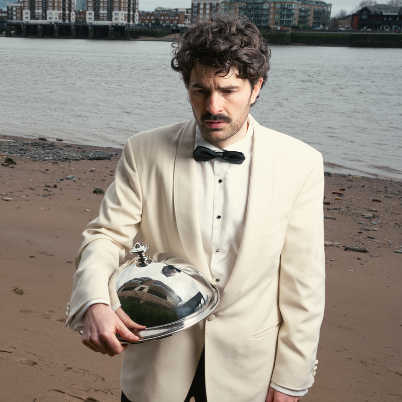 Paddy holding a cloche looking distraught on a bleak beach