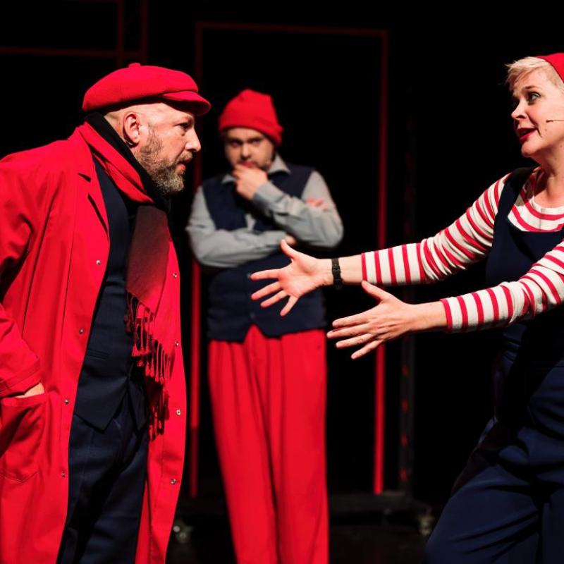 Photo showing performers in red clothing, gesturing to each other