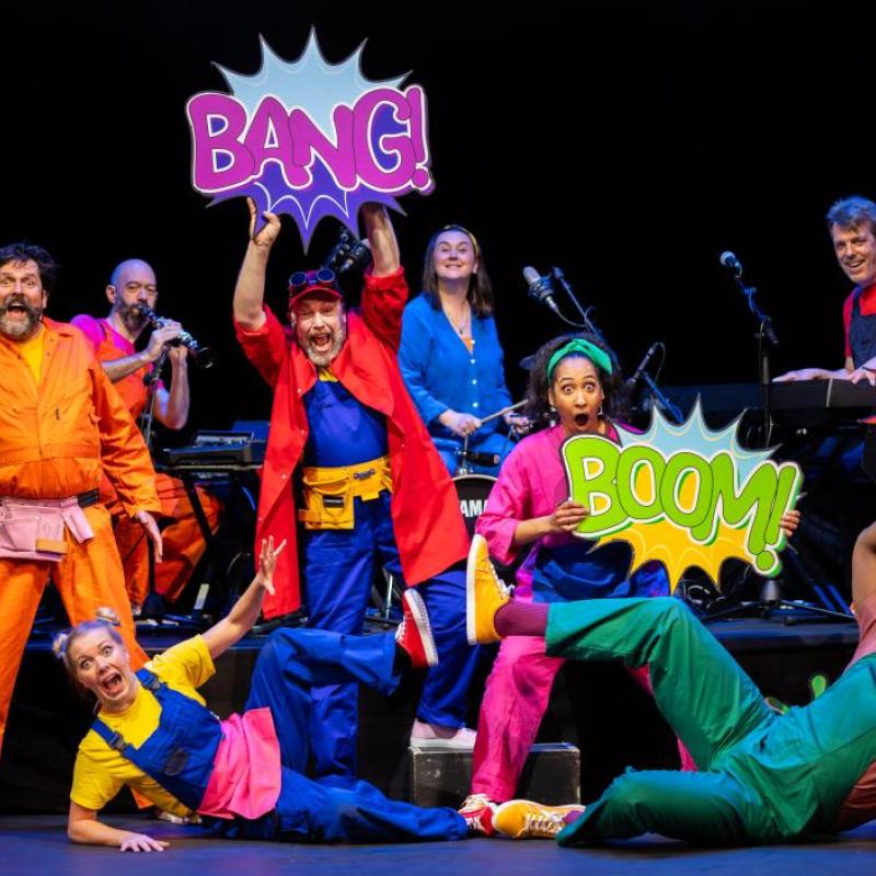 Photo showing group of performers holding signs with cartoon words such as 'BANG!' and 'POW!"
