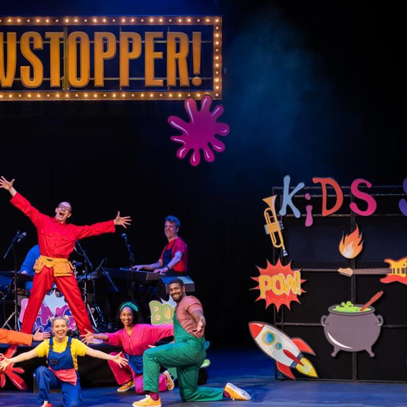This image shows the performers on the left underneath the 'Showstopper!' sign, with the 'Kids Show' sign to the right with all props