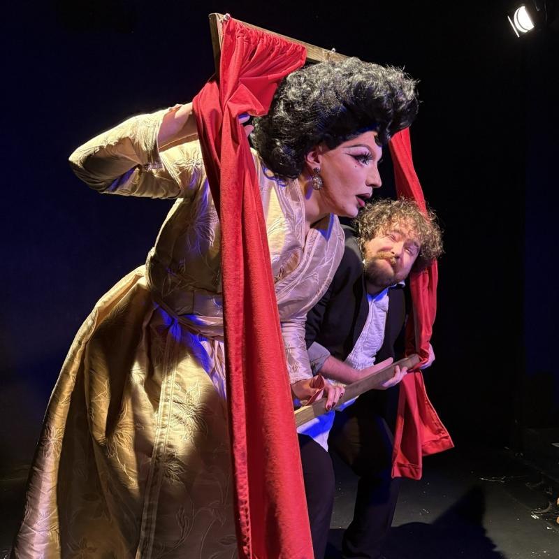 A victorian drag-queen and her hunchbacked servant start out a red-curtainered frame at a new visitor to the castle.