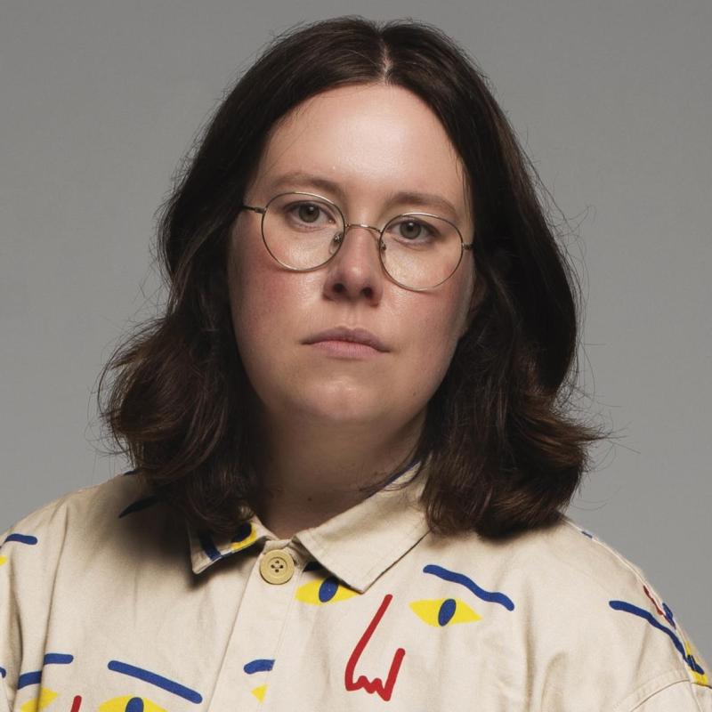 Chloe with a blank expression, wearing a shirt with an artistic pattern. 