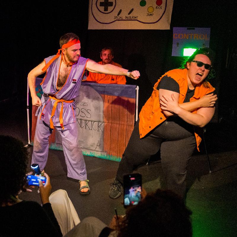 A performer dressed in a karate uniform mid punch whilst someone winces in pain.