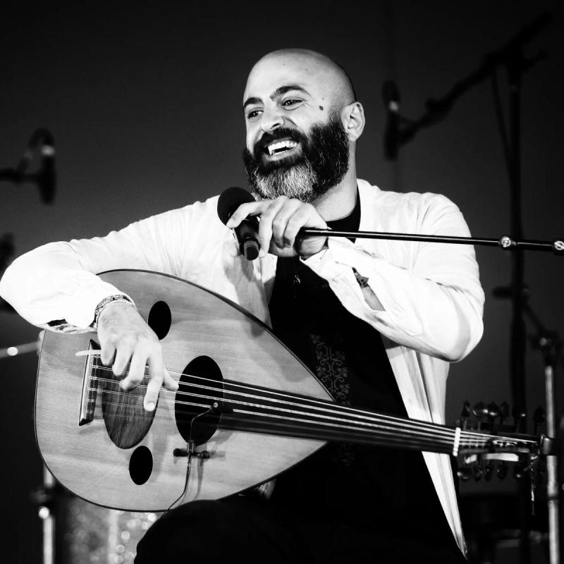 A black and white image of Saied sits behind a musical instrument in front of a microphone