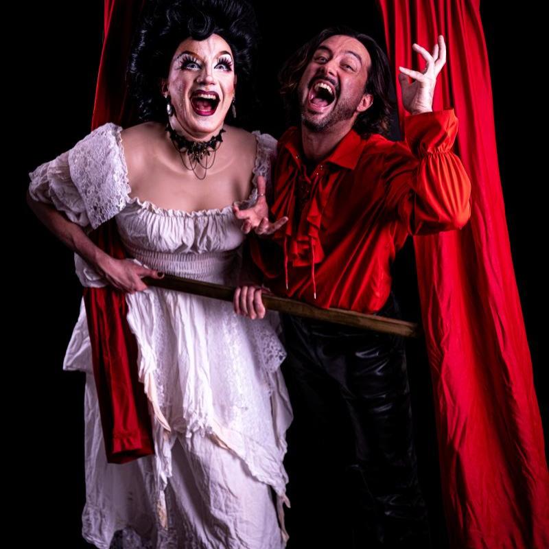 The performers huddle together around a window frame prop in front of a black background.