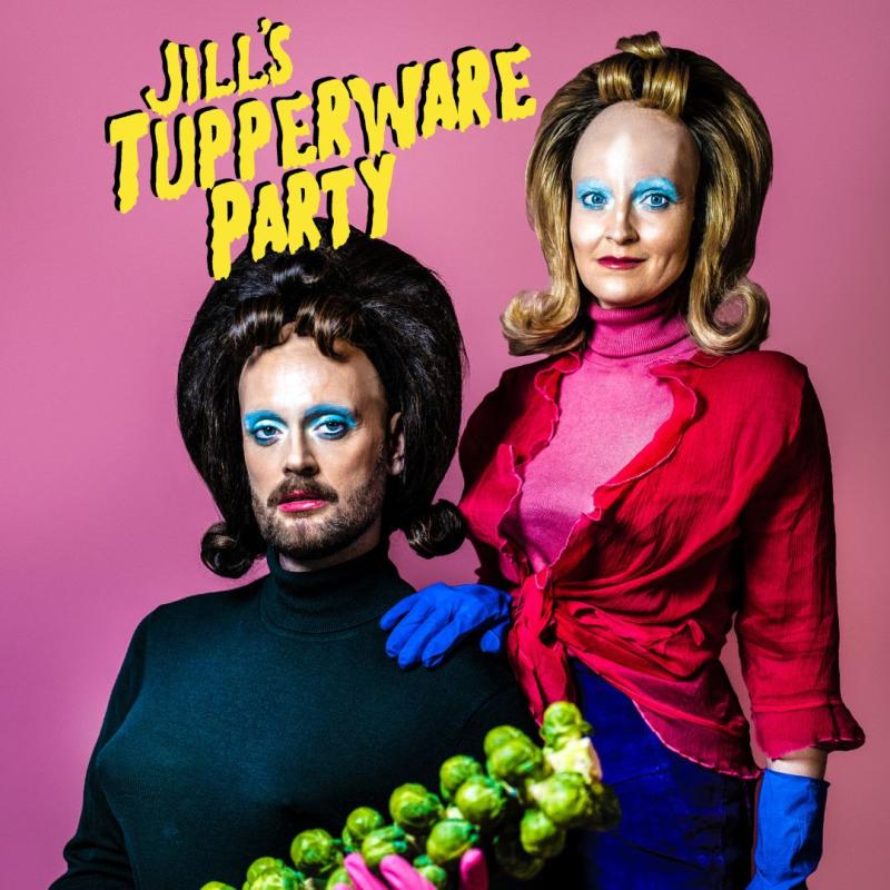 An 80s style couples image. One person is seated in front of the other person, who stands behind them with a hand on their shoulder. They are both wearing big wigs with curled fringes, rubber gloves, and blue eyeshadow.