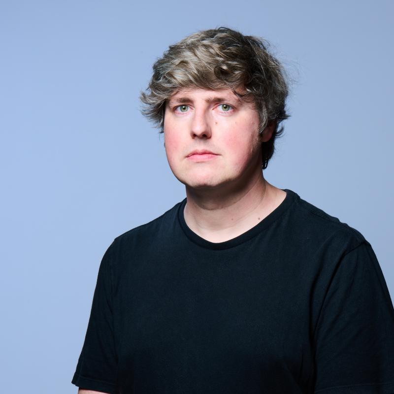 A picture of Glenn, wearing a black t shirt, against a light blue background.